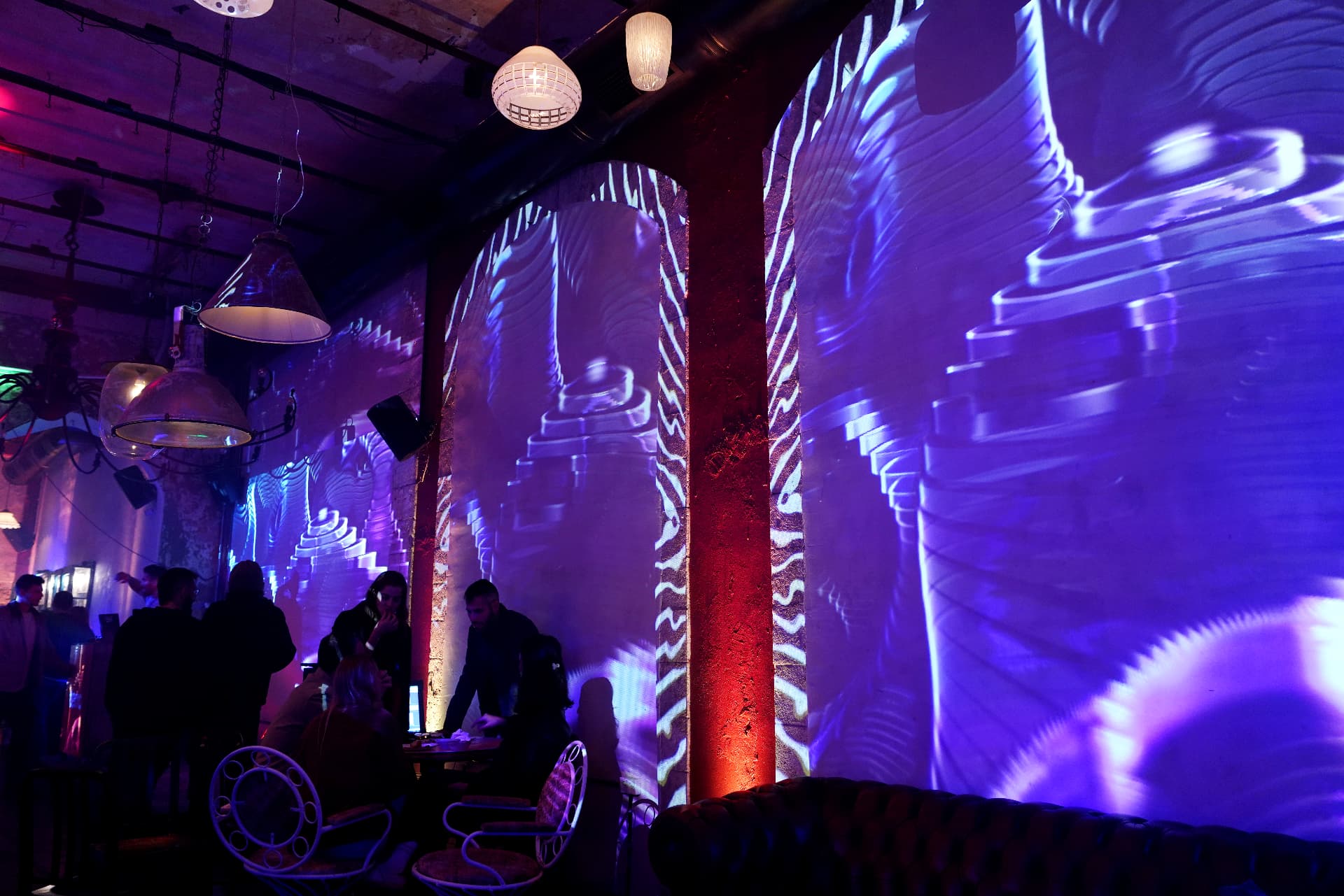 Wide view of brick arches projected with blue spiral patterns, columns lit red, and guests in silhouette