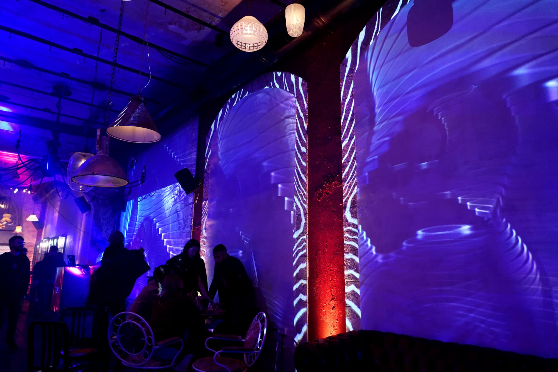 Wide view of an event venue: brick arches and walls projected with blue wave patterns, guests seated at tables