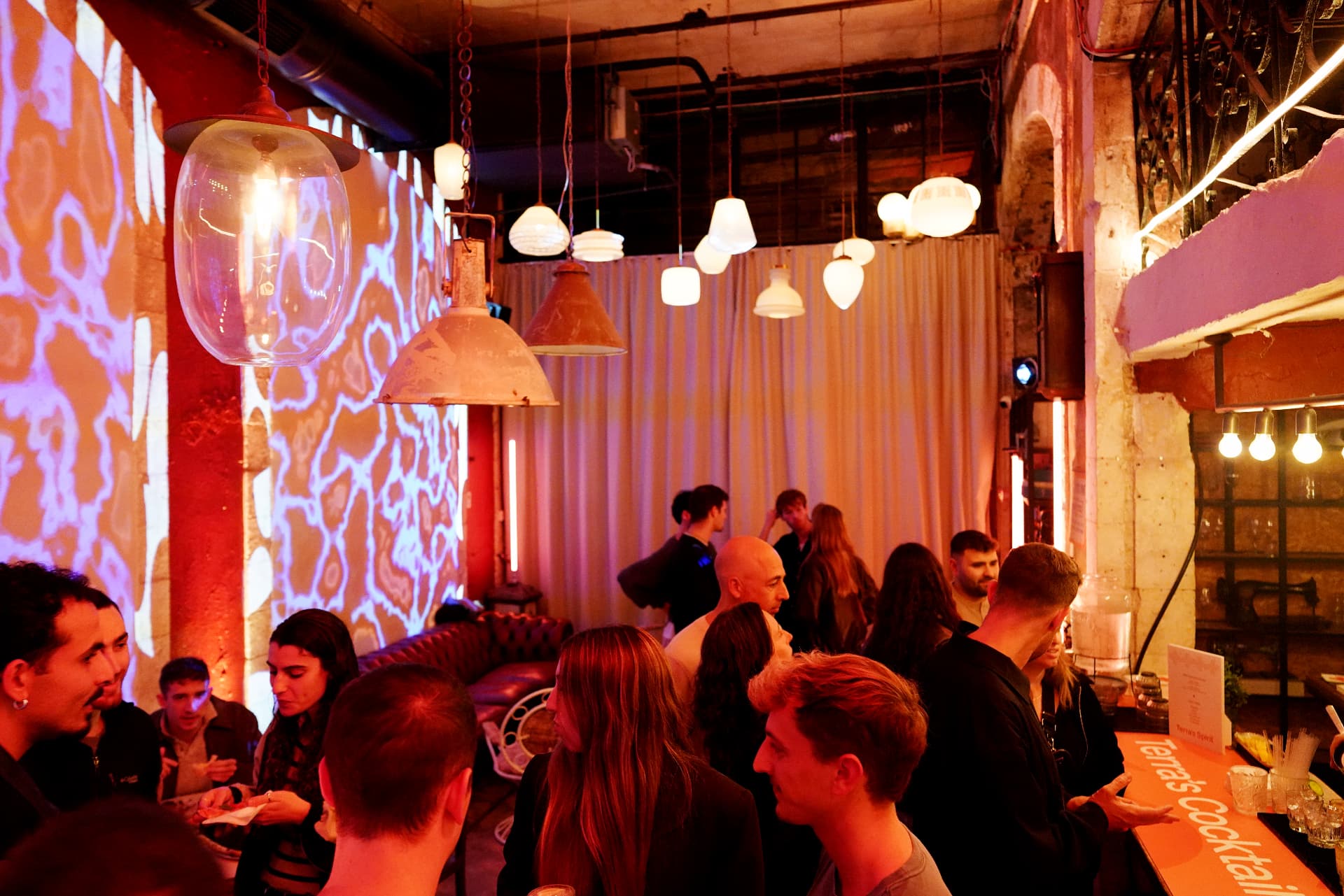 Guests around a bar in warm red light, with a blue projection inside a brick arch