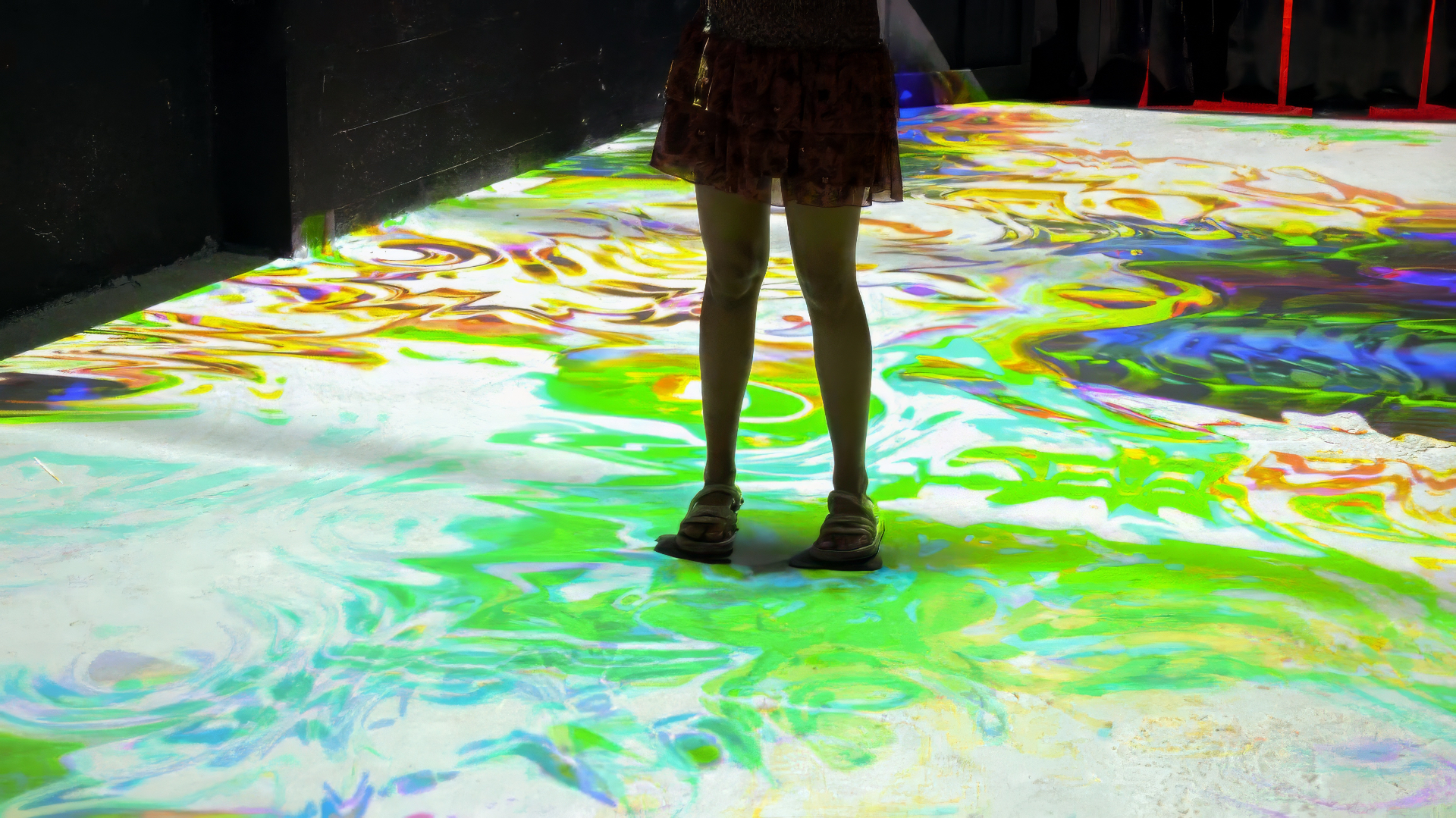 A visitor standing on a floor projected with green, yellow and purple patterns