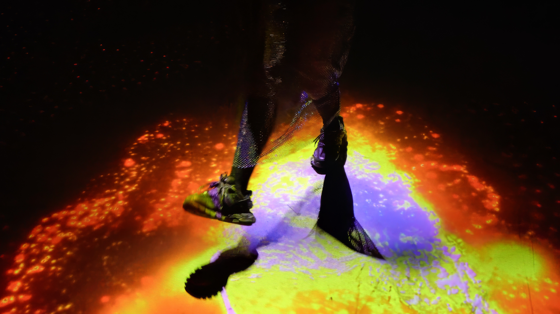 A visitor's feet in motion over a yellow and purple patch of light on the Slices floor