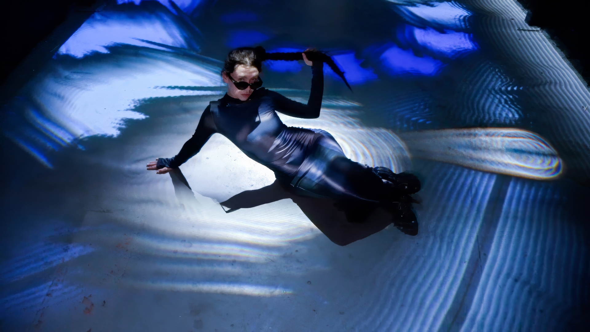 A woman in sunglasses lying on a floor projected with blue and white patterns